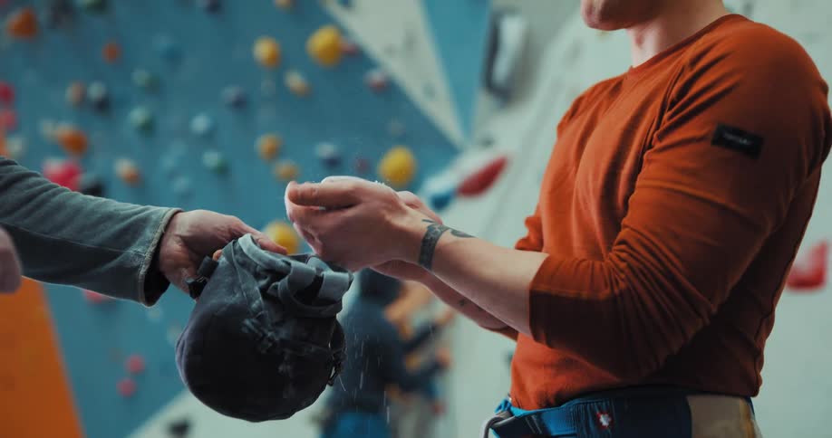 A man puts powder on his hands by the rock climbing wall
