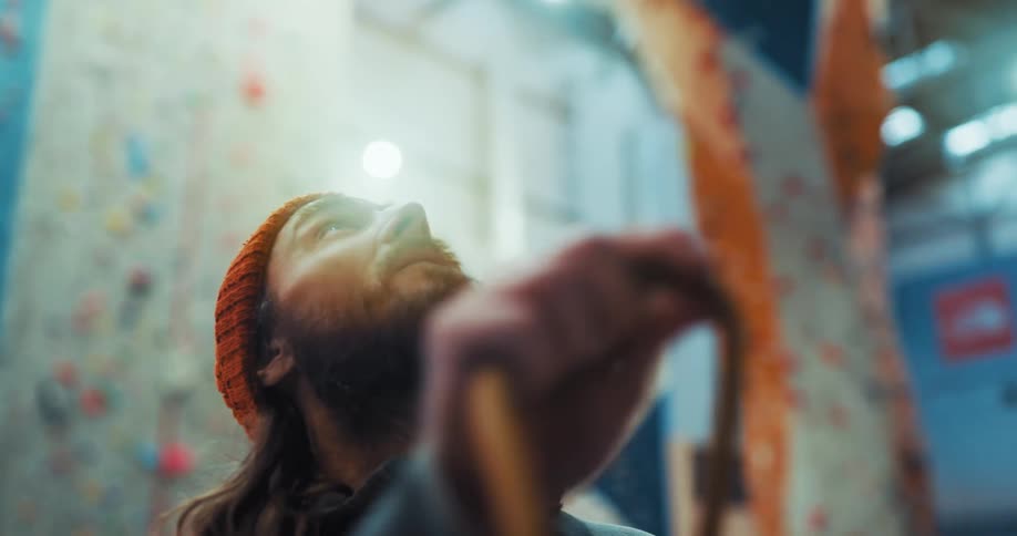 A man is looking up at a climbing wall as he speaks and points