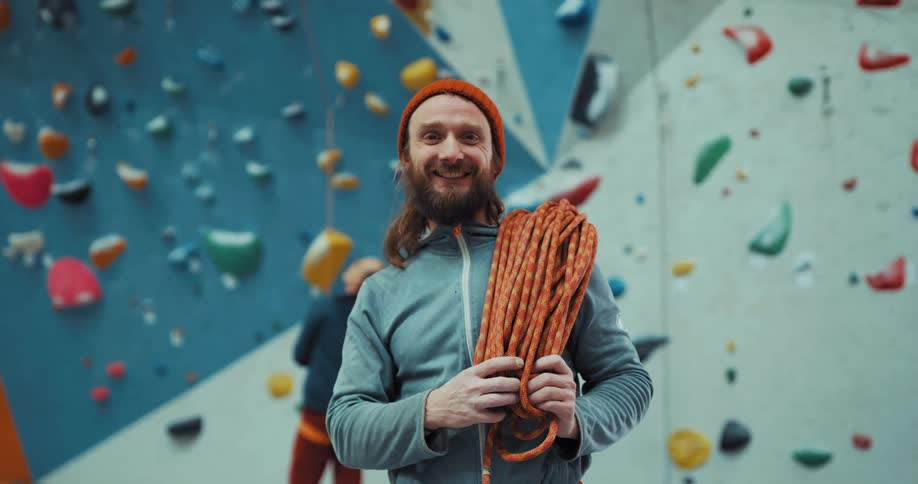 Man holding rope looks up toward top of climbing gym walls before smiling