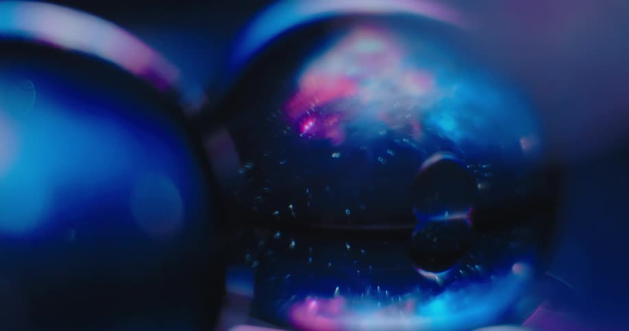 Small light spots move across bubbly surface of blue and pink sphere sitting next o another balls