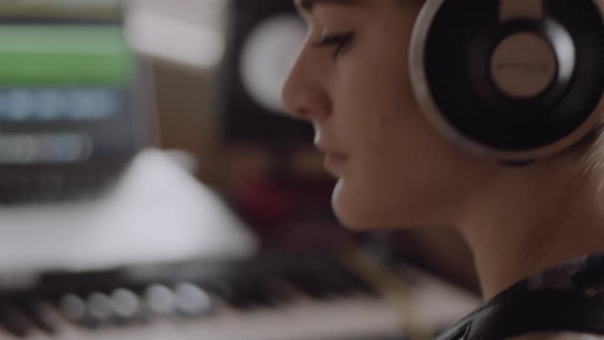 A woman wearing headphones plays the guitar