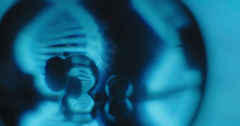 Glowing models of dna are turning inside a dark circle and their reflection shines inside small spheres