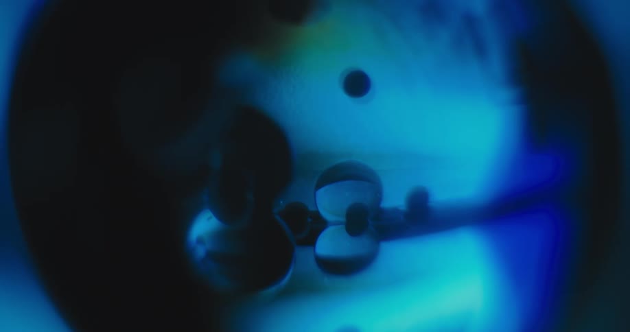 Blue and purple light glows in the distance as the reflection of clear orbs shine in other clear orbs as a bright light goes off and on