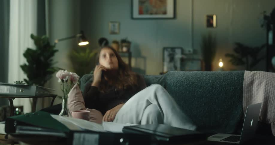 Woman sits on couch working then resting while seeming tired and sad at moments