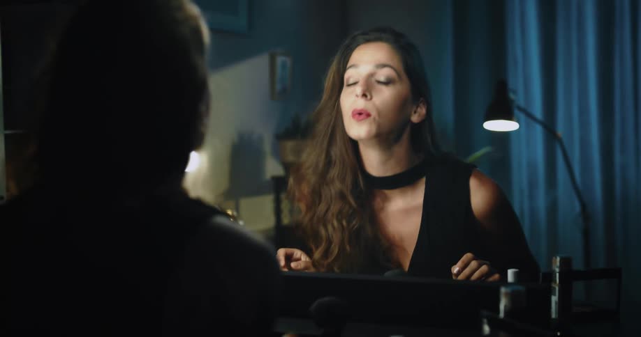 A woman looking at herself in a mirror checking her makeup and opening a makeup bag