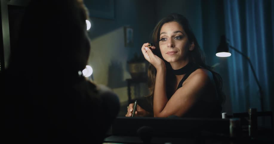 A woman putting on eye makeup in a mirror and smiling