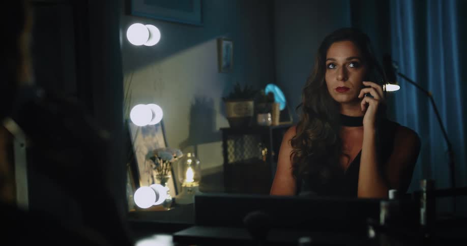 A woman is holding a phone and talking while looking at herself in the mirror she has a smile on her face as she converses with the person on the other end of the line