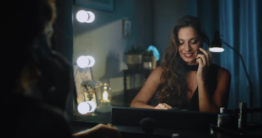 A woman picking up and talking on her cell phone while looking at herself in the mirror smiling and laughing