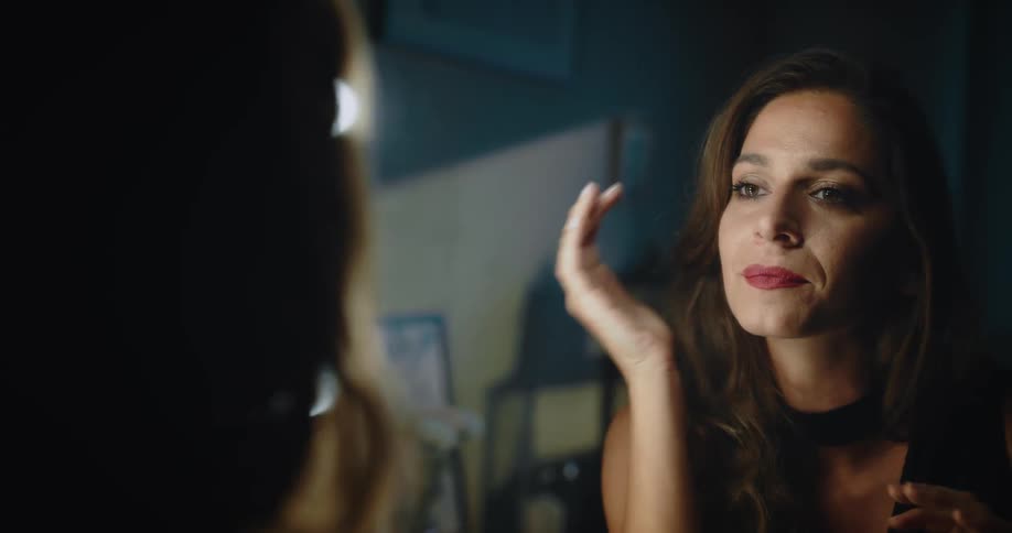 A woman stares at herself in the mirror while answering her smartphone