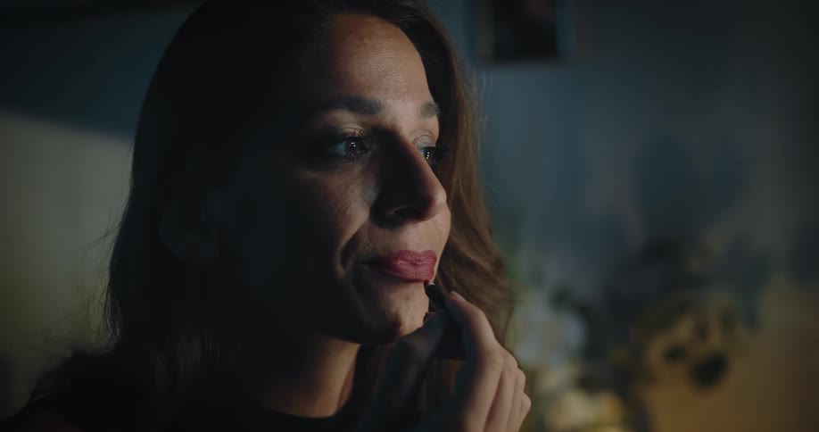 Woman looking in mirror while putting on makeup specifically red lip liner over red lipstick getting ready
