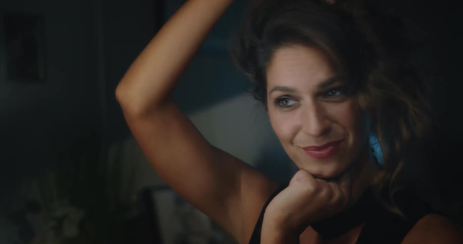 A woman smiles and stares into a mirror while holding her hair up with her hands