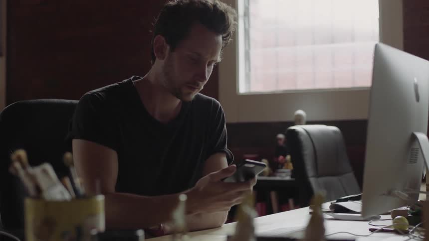 Man types on his keyboard and picks up his phone