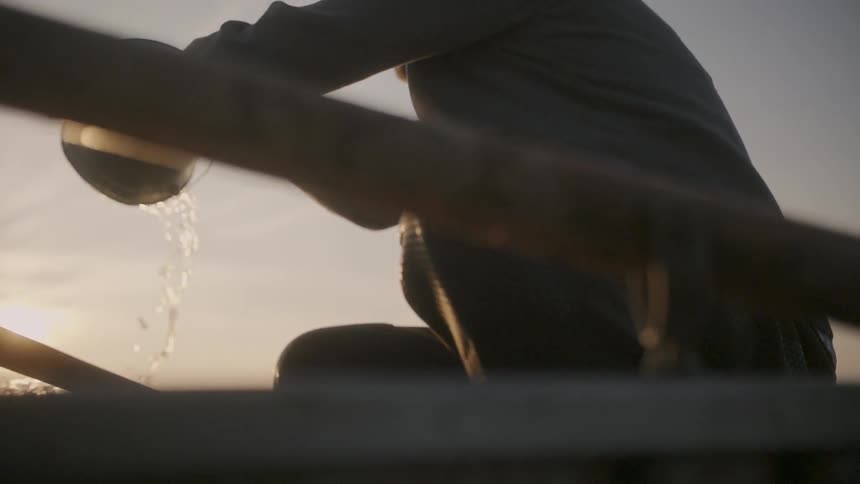 A man dumps a bucket overboard at sunset
