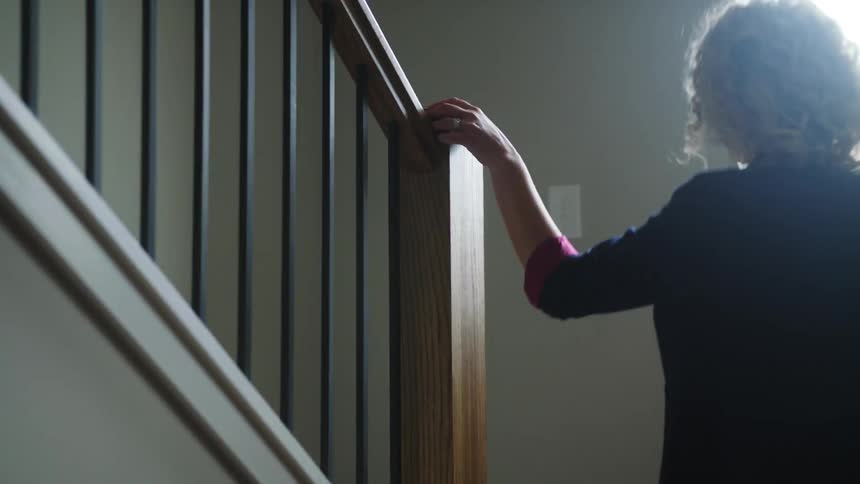 A woman sets her purse down on a side table and walks up the stairs in her house