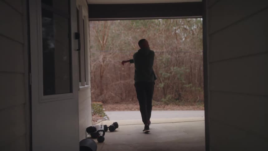 Man exits house then walks to road across from woods before setting off in a jog