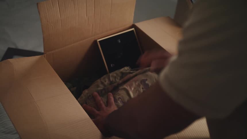 One man packing a moving box with clothing and picture frame closes box and sets aside