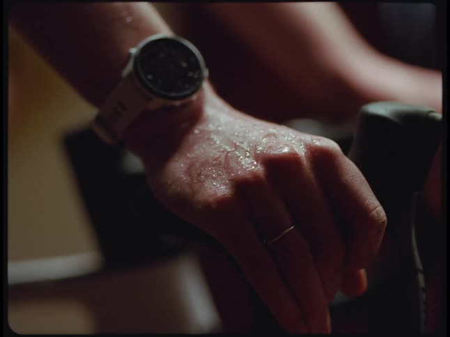Woman wearing ring and wristwatch sweats heavily while pedaling on a stationary bicycle