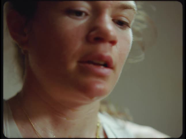 A woman breaths heavily and sweats as she rides an exercise bike and stands up