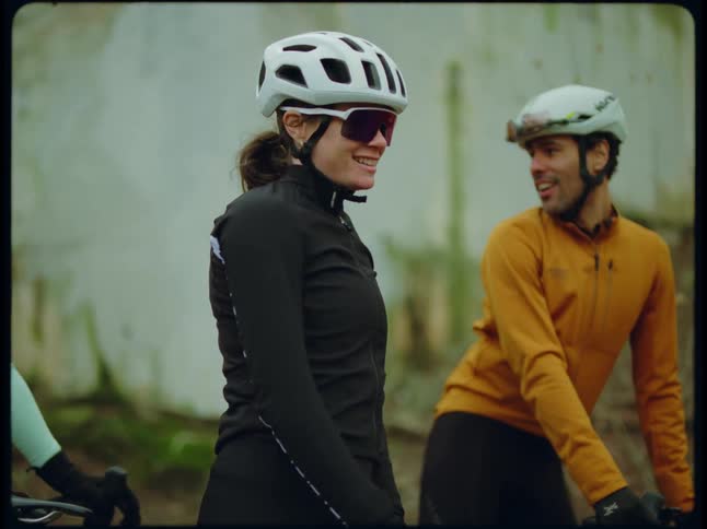 A woman bicyclist wearing a white helmet stopping catching her breath while other bicyclist stop and fist bump her
