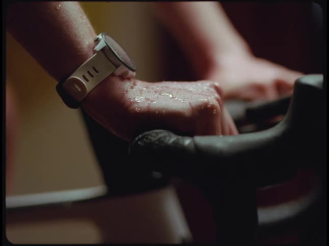 A womans hands sweat as she hold the handlebars of an exercise bike as she pedals