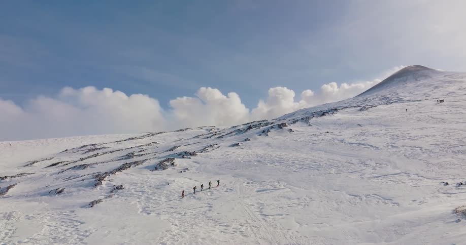 A group of people walk in line up a snow covered mountain