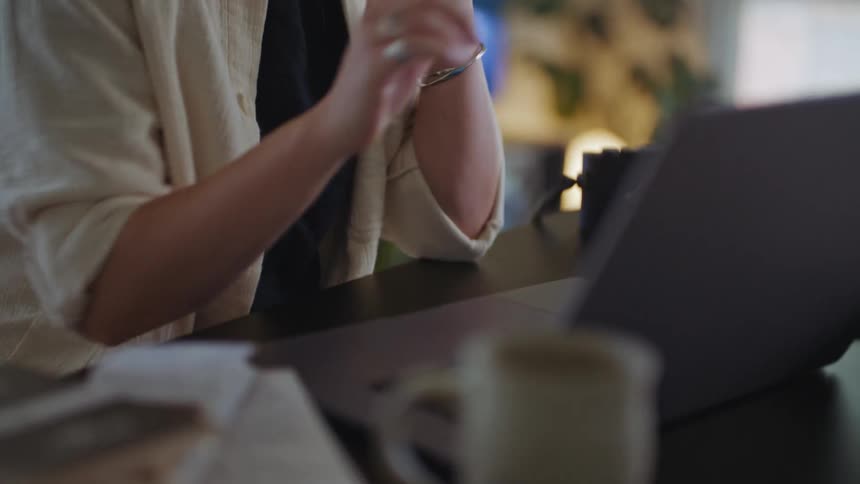A woman is sitting at a desk working on a laptop computer and she smiles as she talks on her phone