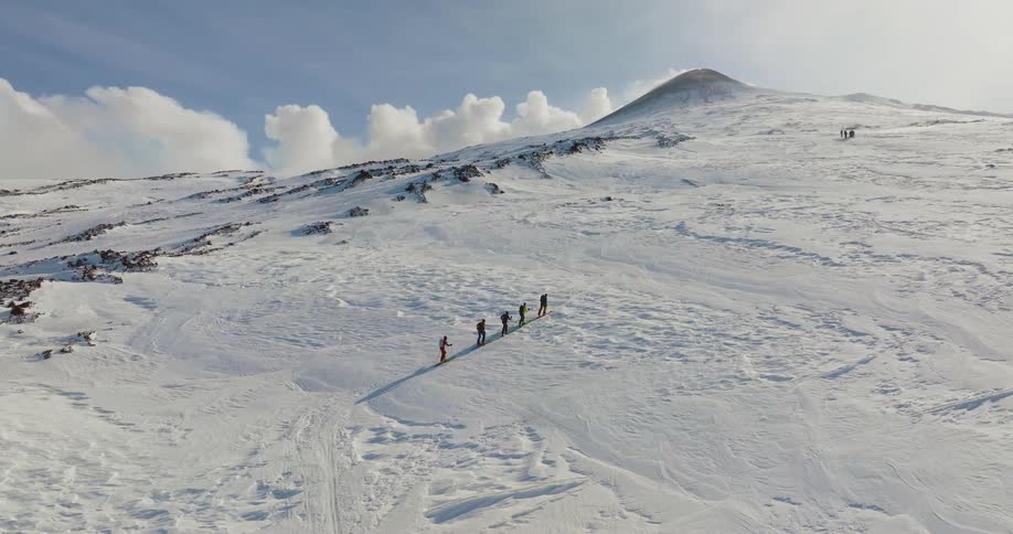 An aerial of a small group of people hiking up a snow covered mountain