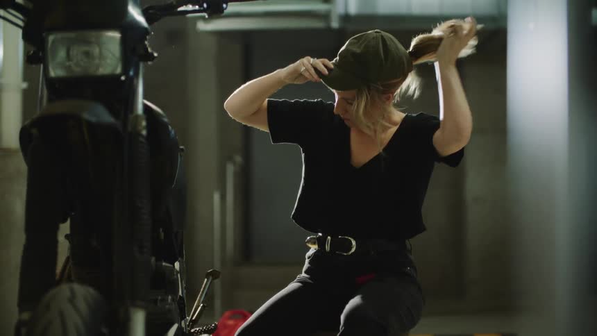 A woman puts on a baseball cap before working on her scooter
