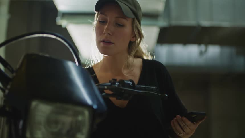 A woman checks her phone as she stands near a parked motorcycle