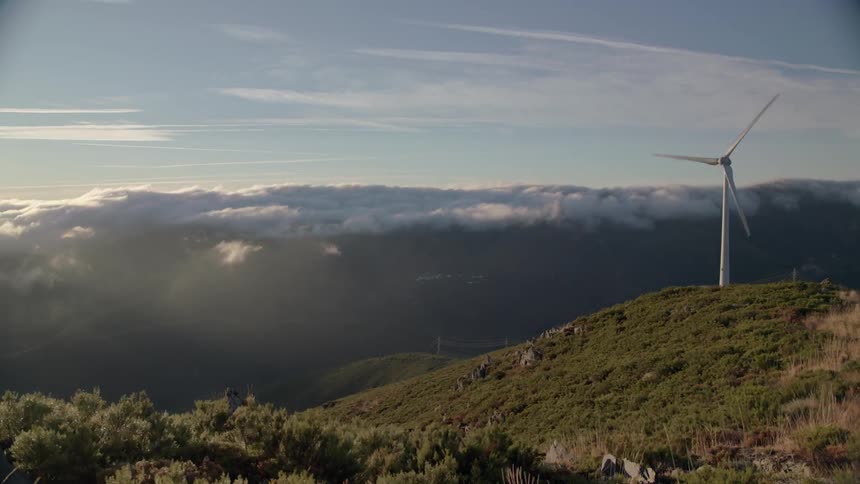 A wind turbine is whirling as clouds swirl around and away from the peak it occupies