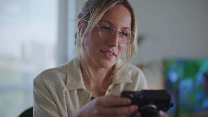 A woman looking at a camera in her hands and smiling then looking away form it