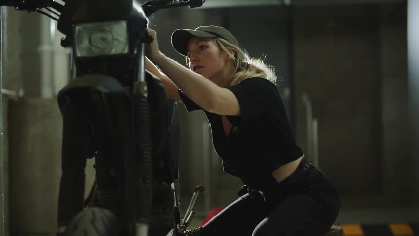 A woman kneels while making adjustments to a motorcycle using a tool