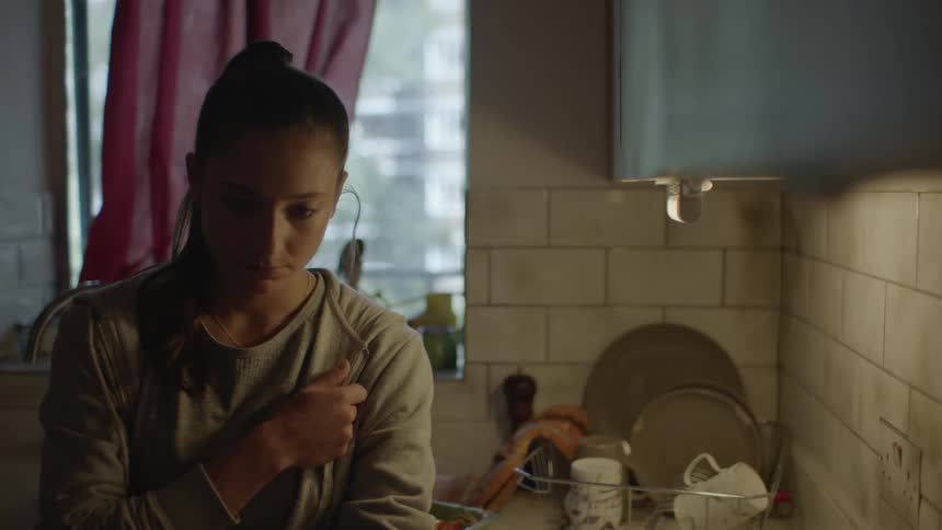 A young woman stands in the kitchen looking dejected and sad