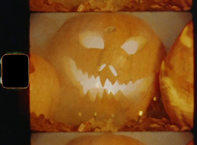 Genuine 8mm film footage zooming out of three lit up jack-o-lantern pumpkins during a Halloween or all hallows evening holiday celebration on a foggy autumn evening with a creepy and scary vibe causing fear and discomfort