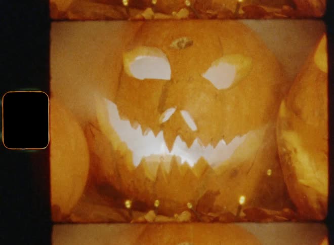 Creative handheld dynamic 8mm film footage of a trio of spooky jackolanterns with the focus on the center one which has a terrifying grimace and a candle inside while smiling in an evil and angry way during a dark night