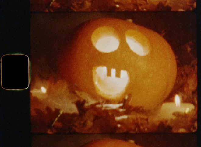 A close up of a carved pumpkin face and then zoomed out to see candles lit next to it laying on the ground surrounded by brown autumn leaves during a cold and dark fall night while celebrating Halloween eve in a traditional way