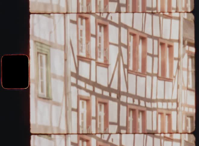 The side of a white building with orange framed windows and wood framing