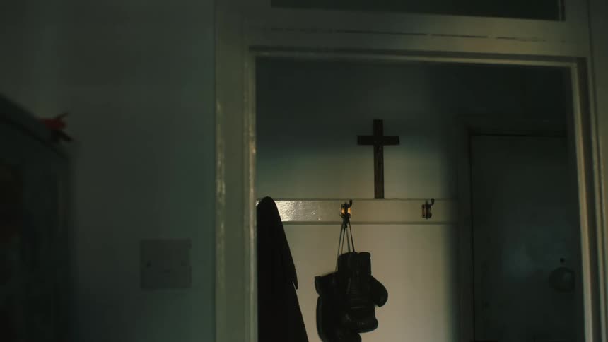 Gloves and a coat hang on hooks underneath a cross in a small closet or entryway