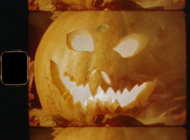 A spooky Halloween pumpkin jackolantern is lit up with smoky mist floating around during a dark autumn night on retro Kodak Super-8 film footage with upward vertical camera movement