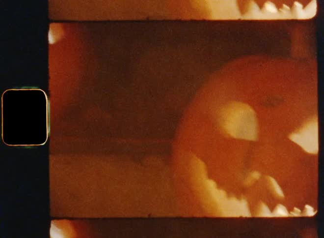 Two lit up jack o lanterns are illuminated with burning candles inside of them while smoke roles over the stairs of a scary Halloween house that is decorated in order to scare children doing trick or treat on vintage 8mm film with a nostalgic vibe