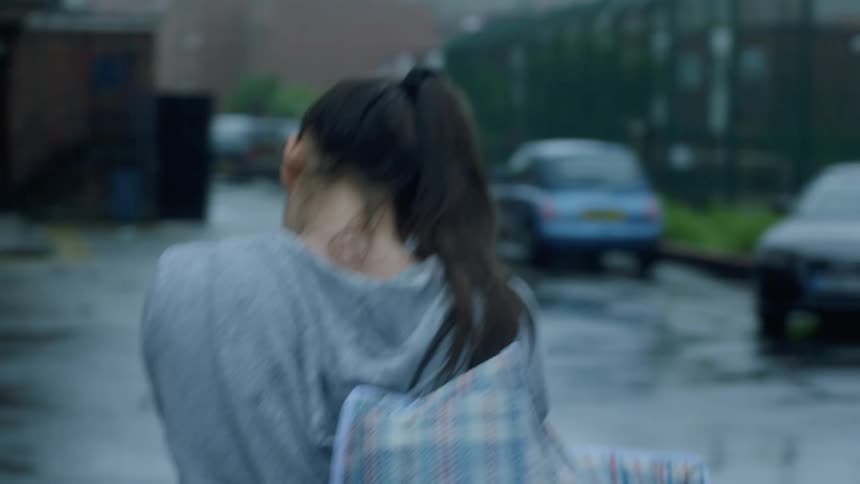 A teenage girl with long dark hair in a ponytail is carrying a bag over her shoulder as she walks on a neighborhood street