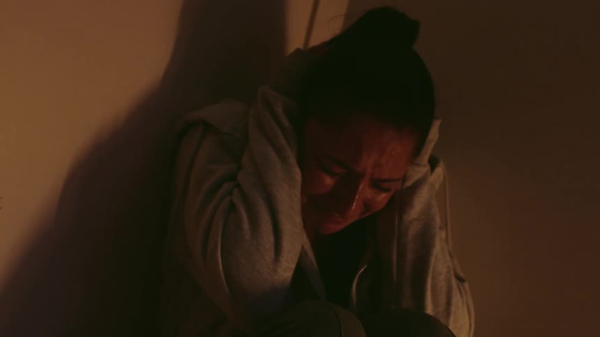 A woman is holding her head and crying in the corner