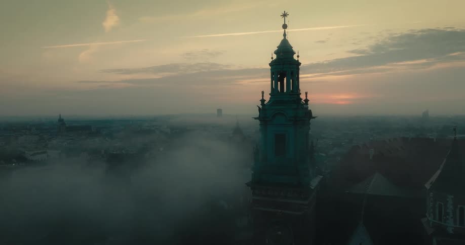Towers with beautiful architecture stand over a crowded foggy city as the sun sets in the distance