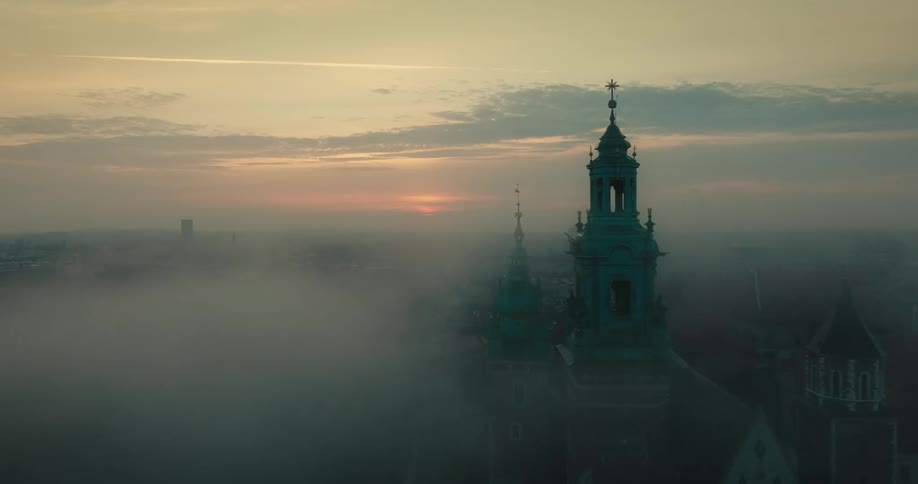 An aerial view of a tall tower cathedral in a city on a foggy evening