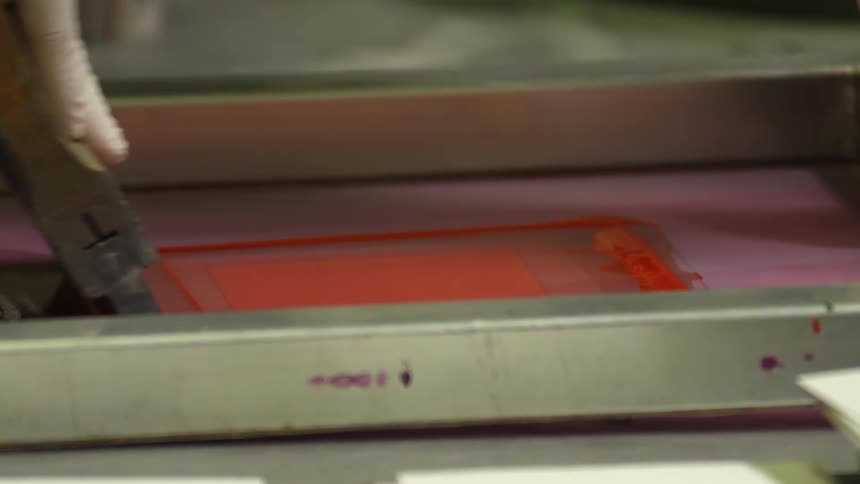 A close up of a persons hands using a scraper to apply paint to a card using a device
