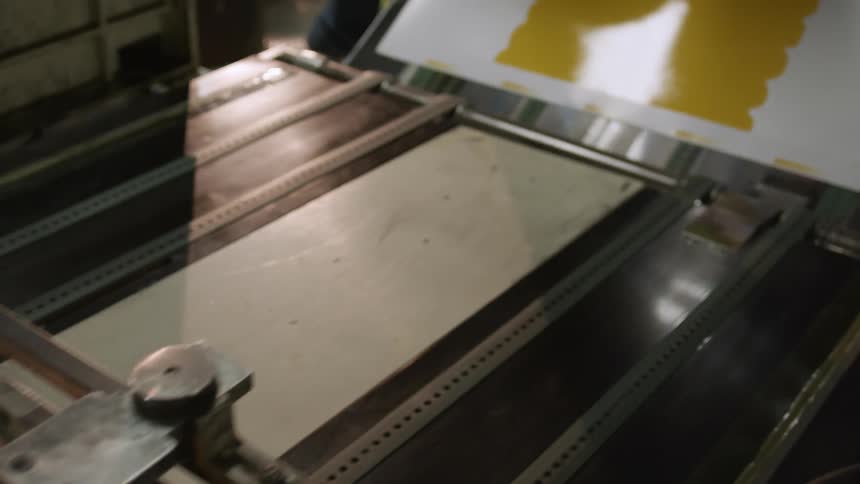 Close up of a printing machine spreading yellow ink over paper moving on a conveyor belt