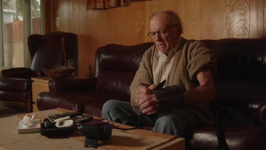 An older elderly man is sitting down indoors