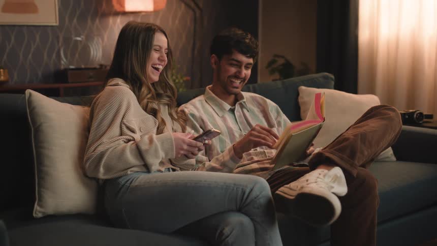 Friends sitting on couch laugh while reading book
