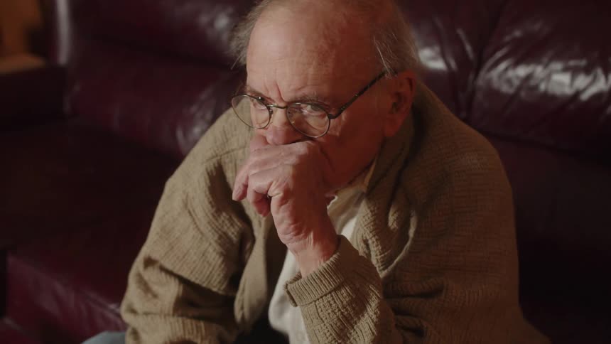 An old elderly man is sitting on the couch