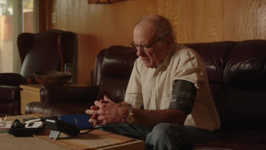 Elderly man using blood pressure machine at home waits on results